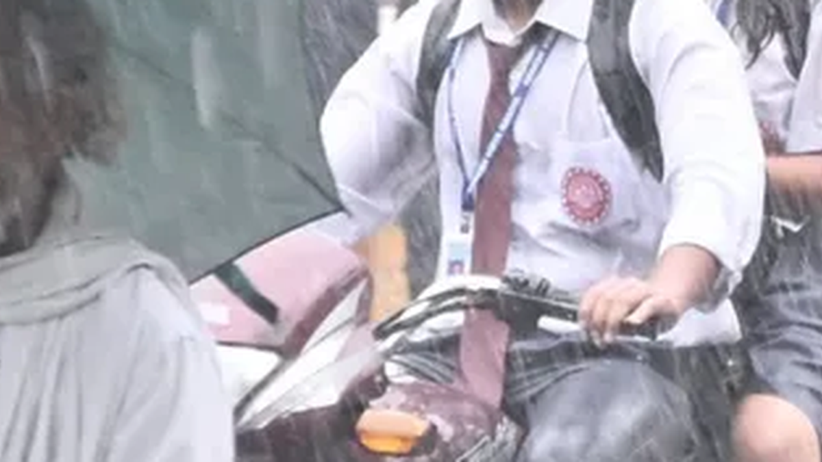 धनबाद में बारिश के बीच सड़क से गुजरते स्कूली छात्र-छात्राएं